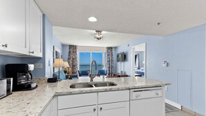 A modern kitchen with a marble countertop, white cabinetry, and a built-in dishwasher.