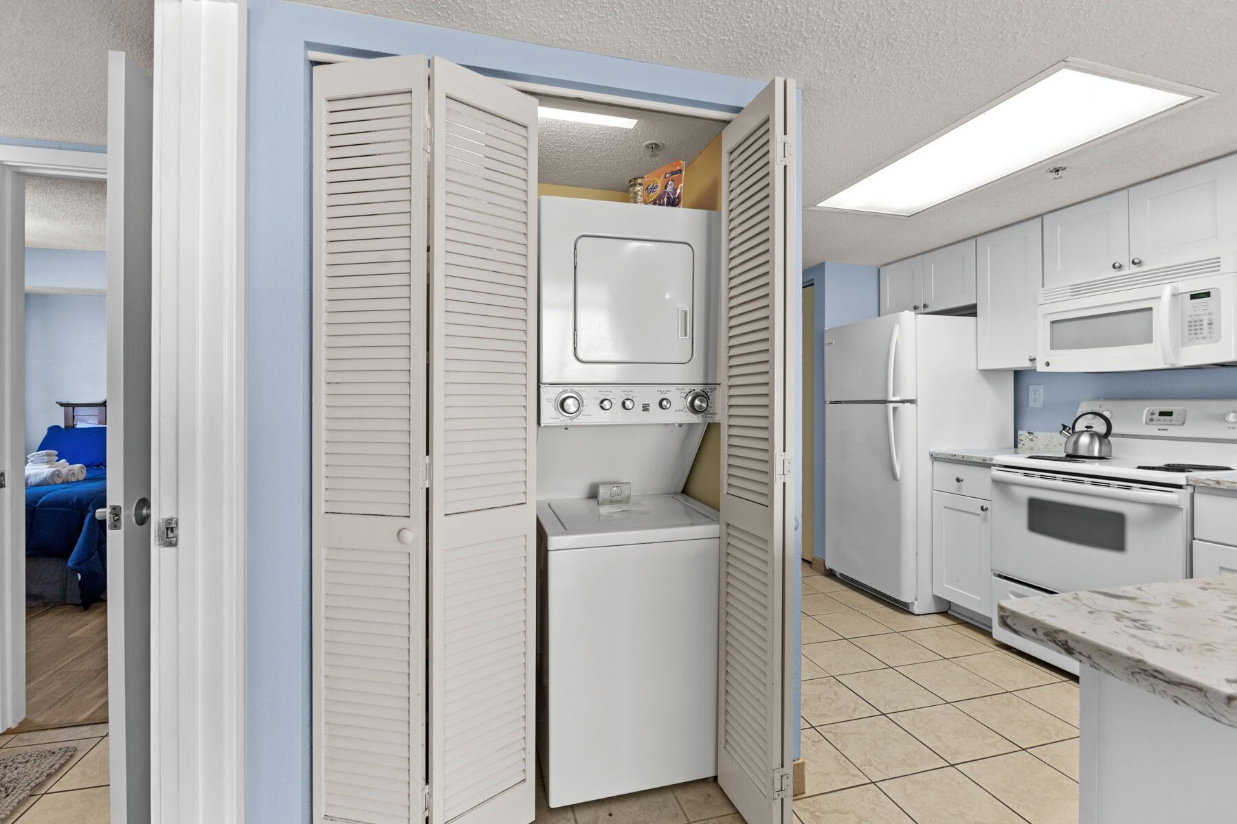 Cocina compacta con microondas, refrigerador y horno. Se observa una lavadora pequeña en la esquina.