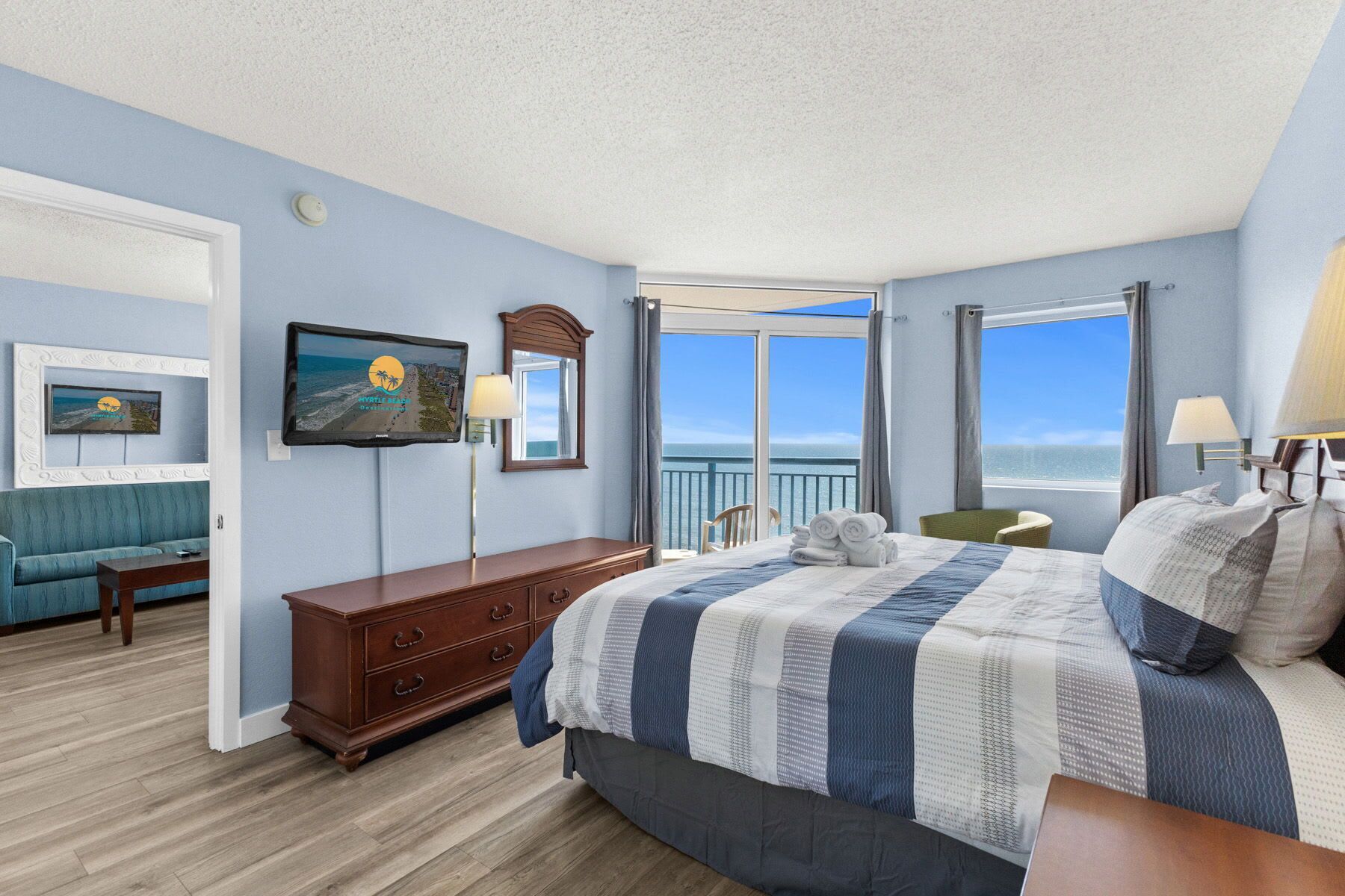 Ein Schlafzimmer mit Bett, Kommode, Fernseher und Blick auf den Ozean.