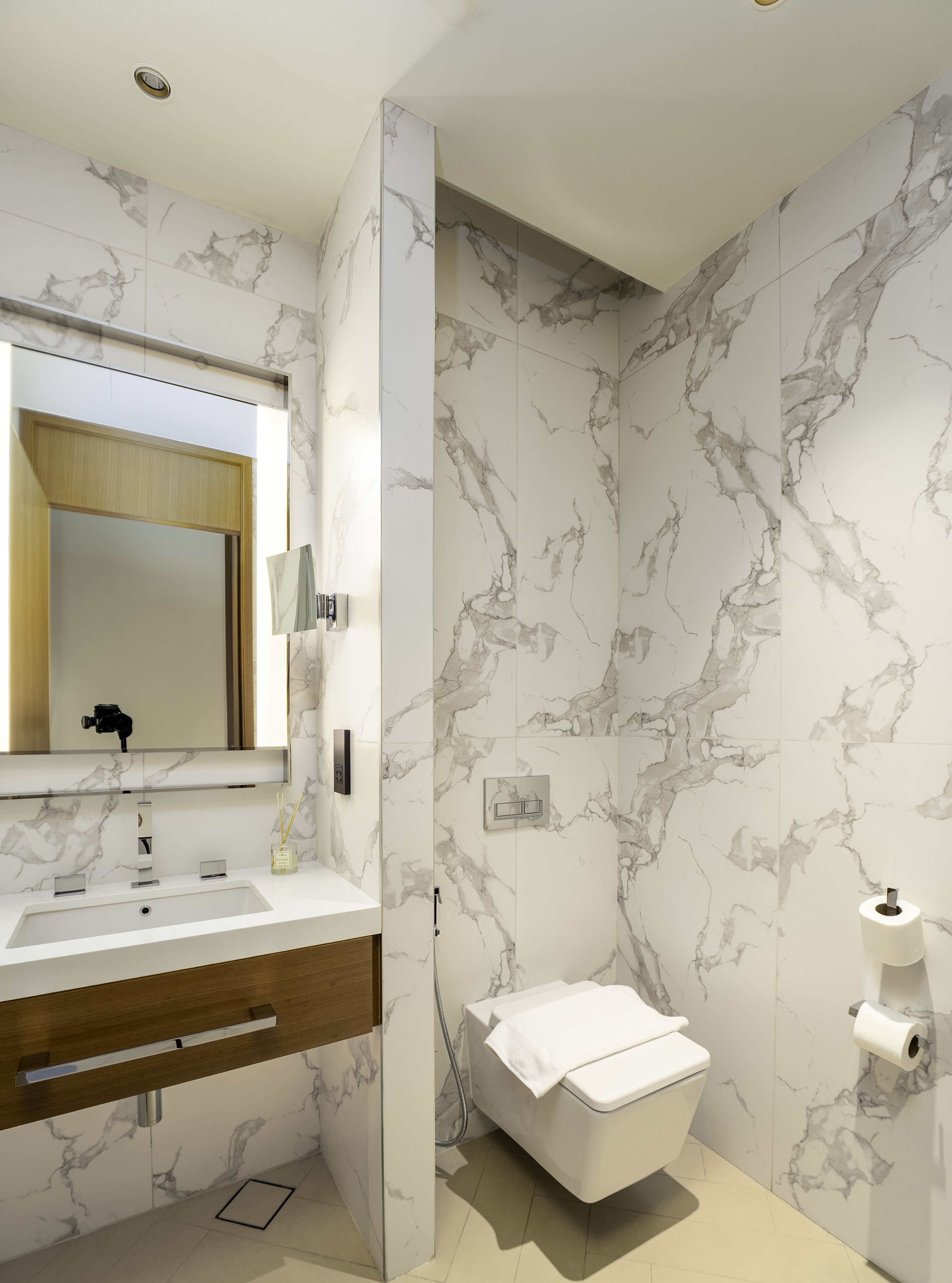 Ein modernes Badezimmer mit Marmorfliesenspiegel, einem Holzbadezimmermöbel, einem großen Spiegel und einer Toilette.