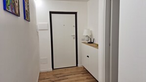 A hallway with a white door, a wall-mounted telephone, a lamp, and a shelf with a lamp and a box. - Charming 1-bedroom apartment in wonderful Palermo with AC, WiFi (Palermo)