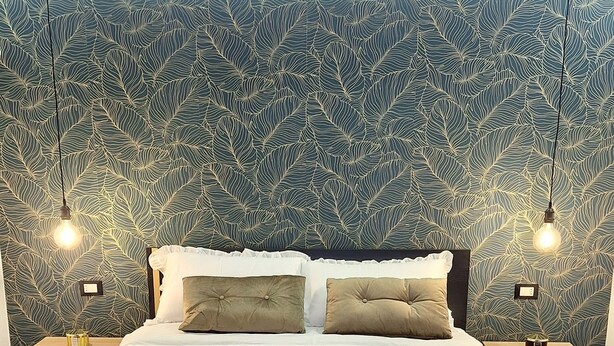 A neatly made bed with a grey duvet, two bedside tables with lamps, and a patterned wallpaper. - Charming 1-bedroom apartment in wonderful Palermo with AC, WiFi (Palermo)
