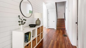 Un couloir doté d’un plancher en bois, d’une console blanche agrémentée de paniers, d’un miroir et d’une lampe.