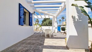 Eine überdachte Terrasse im Freien mit weißen Wänden, blauen Fensterläden und einem Tisch mit Stühlen.