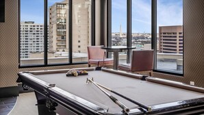 A pool table in a room with large windows, a chair, and a table.