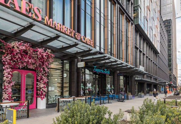 A modern building with a glass facade, a storefront with a pink floral display, and outdoor seating areas.