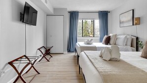 A modern hotel room with a large bed, a TV mounted on the wall, and a window with curtains.