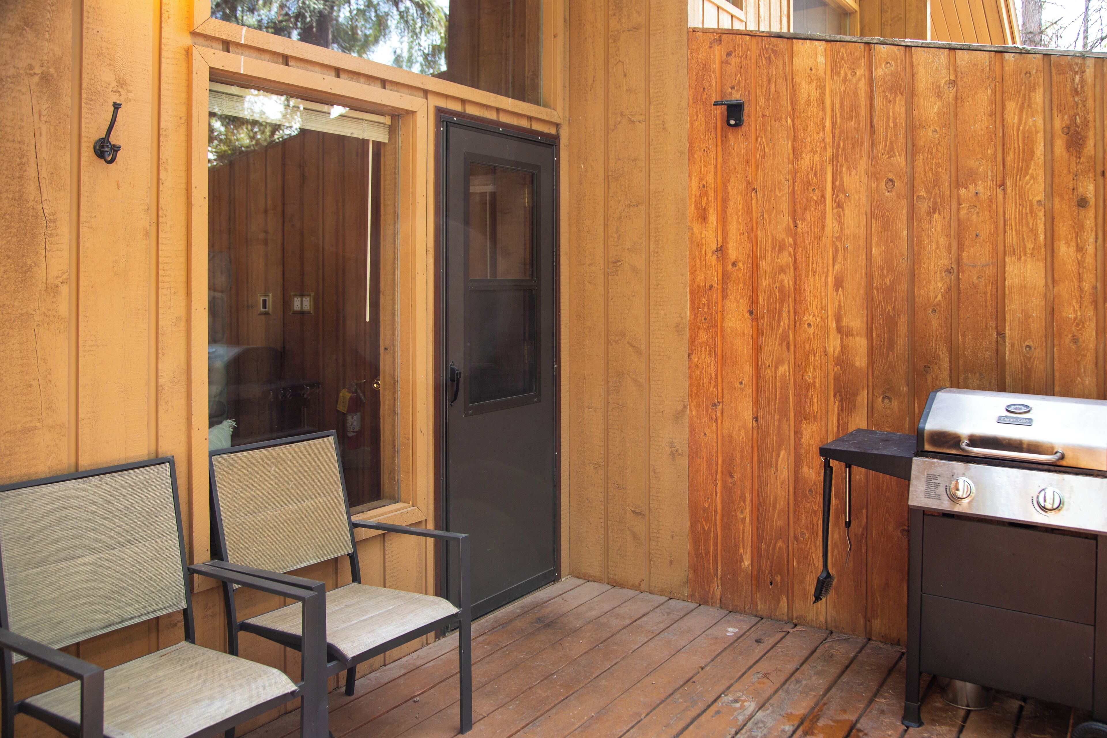 Een houten terras met een barbecue en twee stoelen.