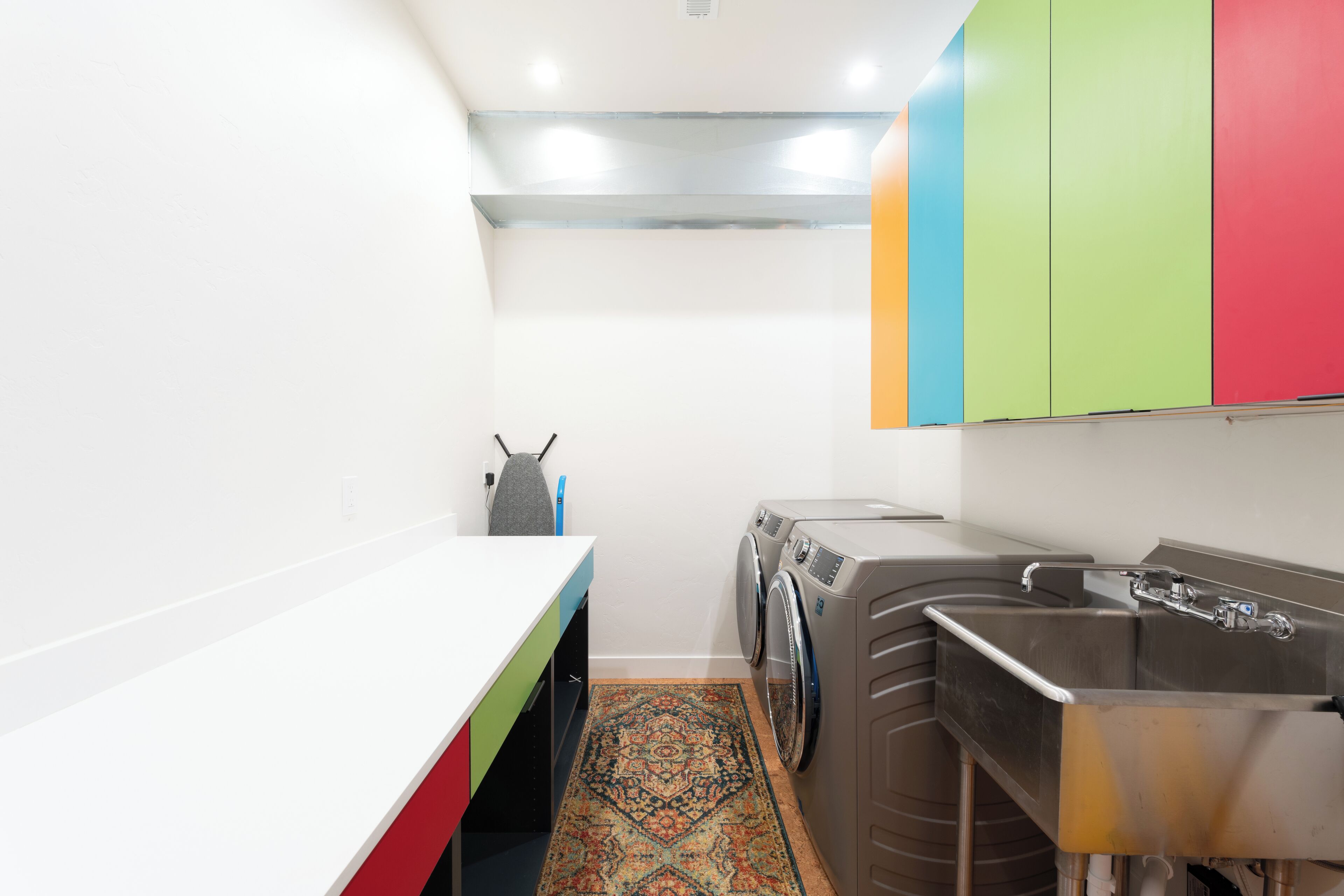 Une petite buanderie comprenant un lave-linge, un évier et un tapis aux couleurs vives.
