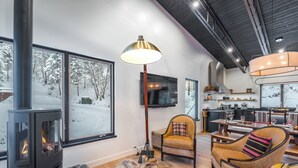 Ein gemütliches Wohnzimmer mit Kaminofen, großen Fenstern mit Blick auf Schnee, einer bequemen Couch und einem Essbereich.