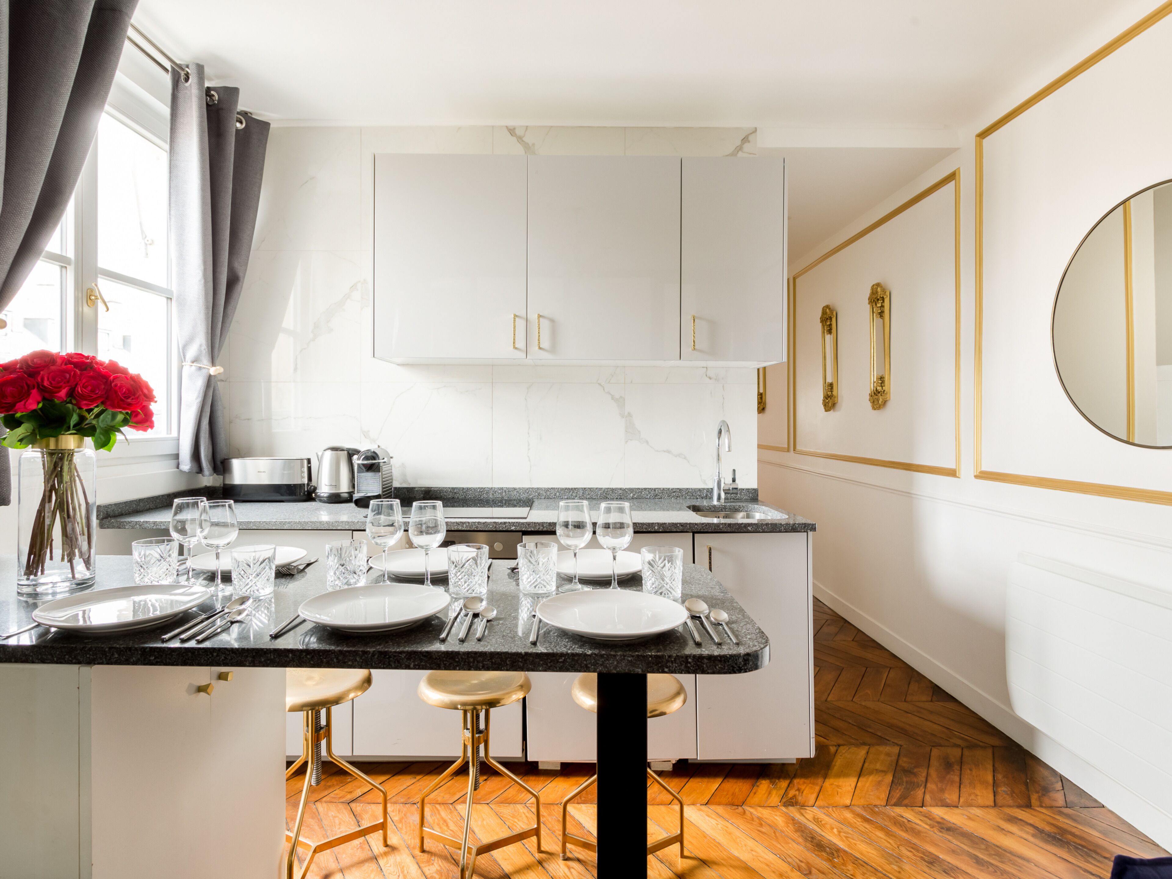 A modern kitchen with white cabinets, a marble countertop, and a dining area with stools.