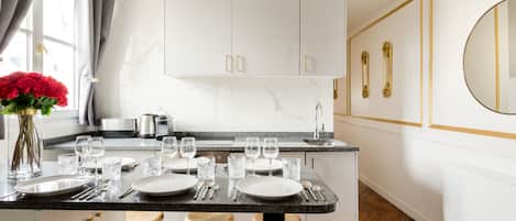 A modern kitchen with white cabinets, a marble countertop, and a dining area with stools.