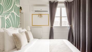Una camera d'albergo con un letto, un condizionatore d'aria a parete, una finestra con tende e una parete decorata con un motivo a foglia verde.