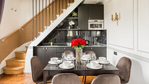 Een eethoek met een tafel voor vier personen, een trap en een keuken op de achtergrond.