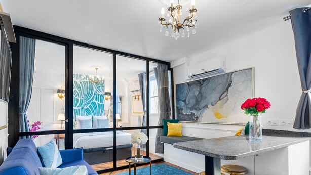 Een moderne hotelkamer met een groot bed, een blauwe bank, een eethoek met barstoelen en een groot raam met uitzicht.