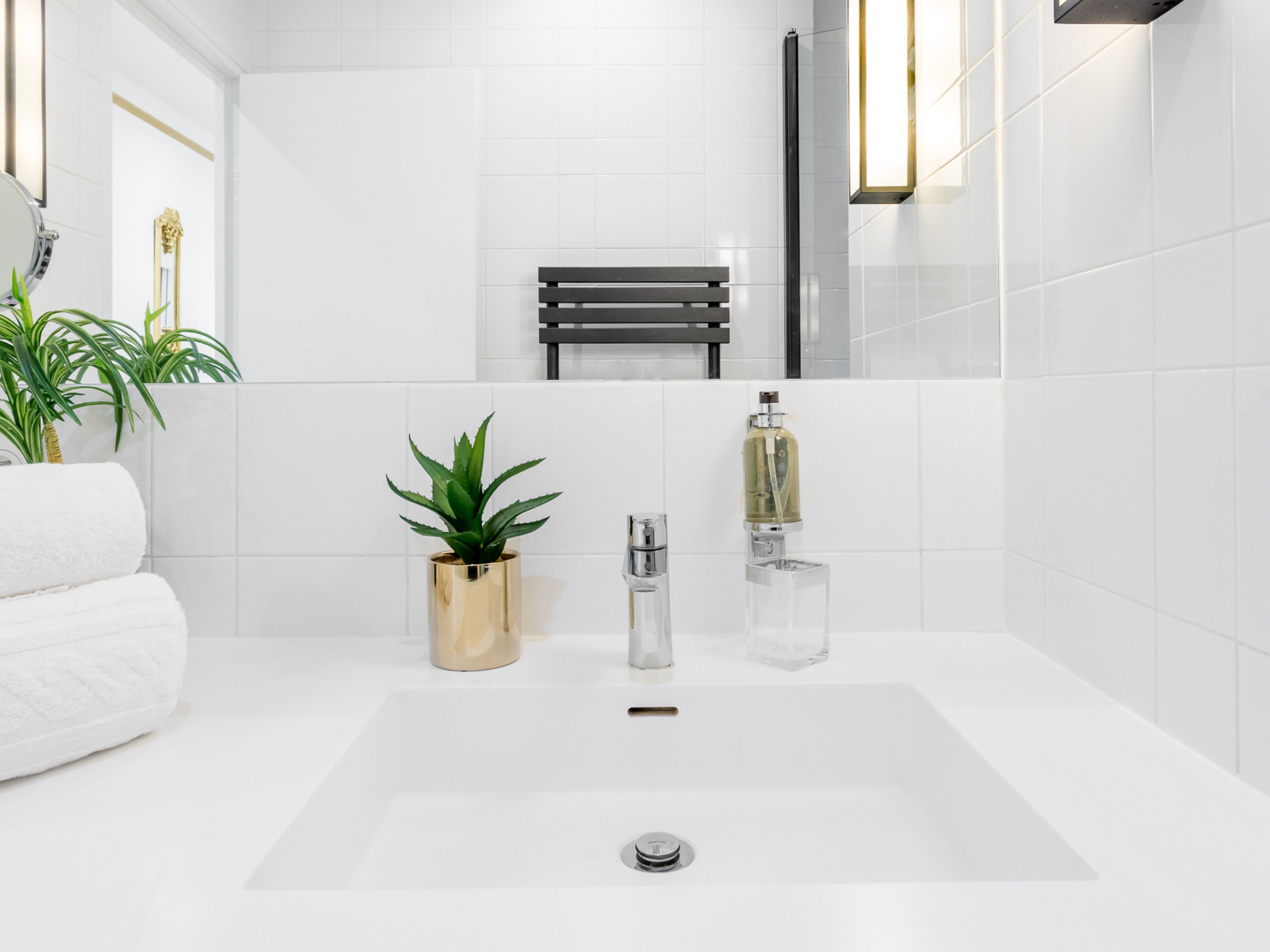 A modern bathroom with a white sink, a gold-colored plant, and a clear glass bottle.