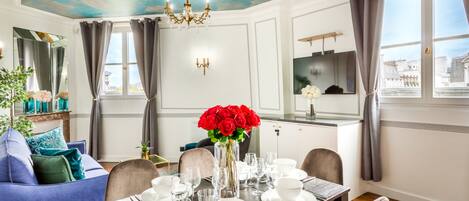 A dining room with a table set for four, a chandelier, and a view of the city through large windows.