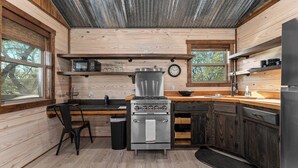 A compact kitchen with wooden walls, a stove, microwave, and a sink. - Broken Arrow - Private Escape, Hot Tub & Fire Pit (Fredericksburg)