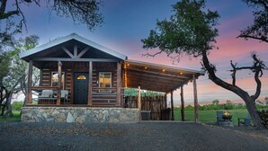 A rustic cabin with a stone foundation, wooden exterior, and a covered porch with string lights. - Broken Arrow - Private Escape, Hot Tub & Fire Pit (Fredericksburg)