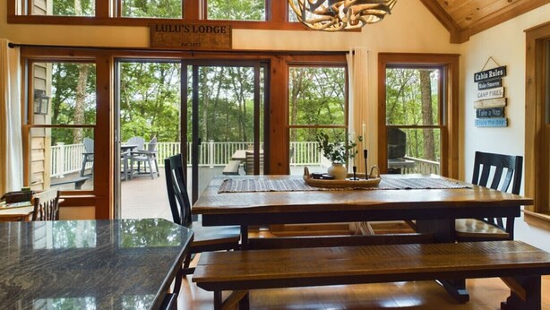 Un espace repas dans un chalet, avec une grande table en bois, des bancs et un lustre.