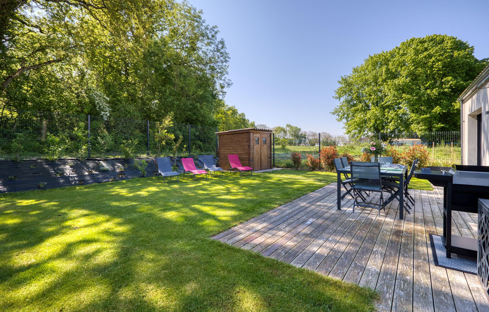 Een achtertuin met een houten terras, een barbecuehoek en een kleine schuur.