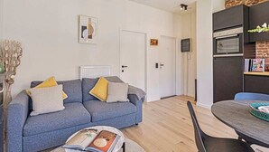 Un salon moderne avec un canapé gris, une table à manger et un coin cuisine doté d’un four encastré.