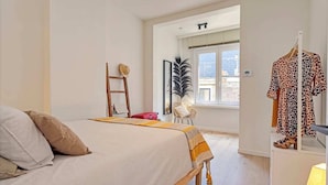 Une chambre avec un lit, une échelle, une chaise, une plante et un portant à vêtements.