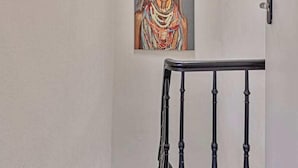Un couloir étroit avec une lucarne, une rambarde noire et un tableau accroché au mur.