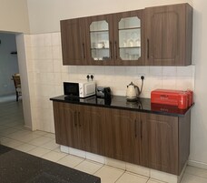 Una cocina con armarios de madera, una encimera negra, microondas, tostadora, hervidor y una caja roja para pan.