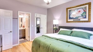 A bedroom with a bed, a nightstand, a ceiling fan, a framed picture, and a door leading to a bathroom.