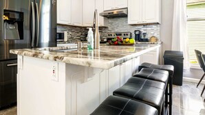 A modern kitchen with white cabinets, a stainless steel refrigerator, a built-in oven, and a marble countertop.