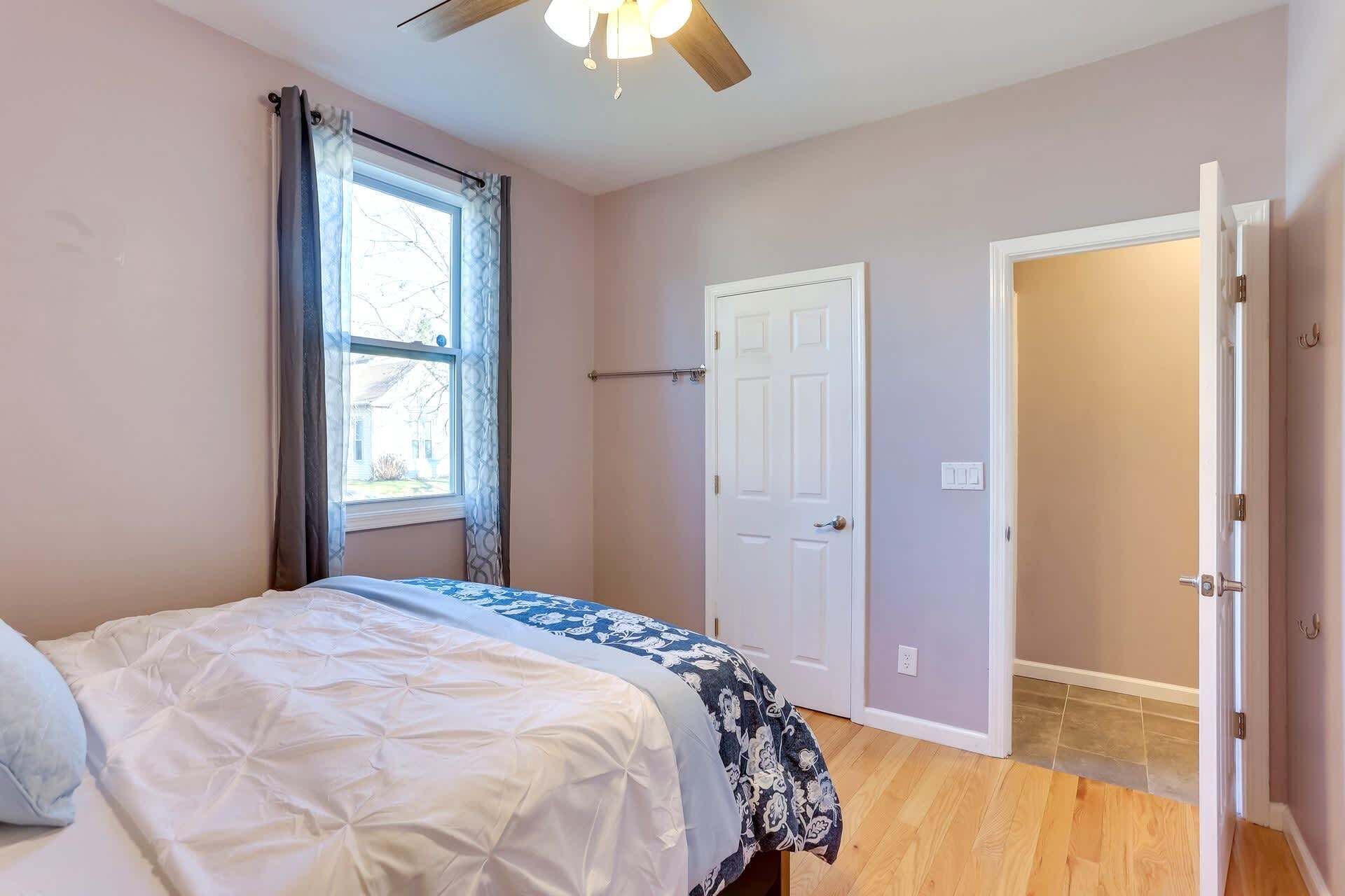 Un dormitorio con cama, ventana con cortinas, puerta y ventilador de techo.