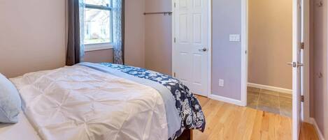 Un dormitorio con cama, ventana con cortinas, puerta y ventilador de techo.