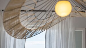 Een kamer met dunne gordijnen, een zichtbaar raam en een hanglamp.