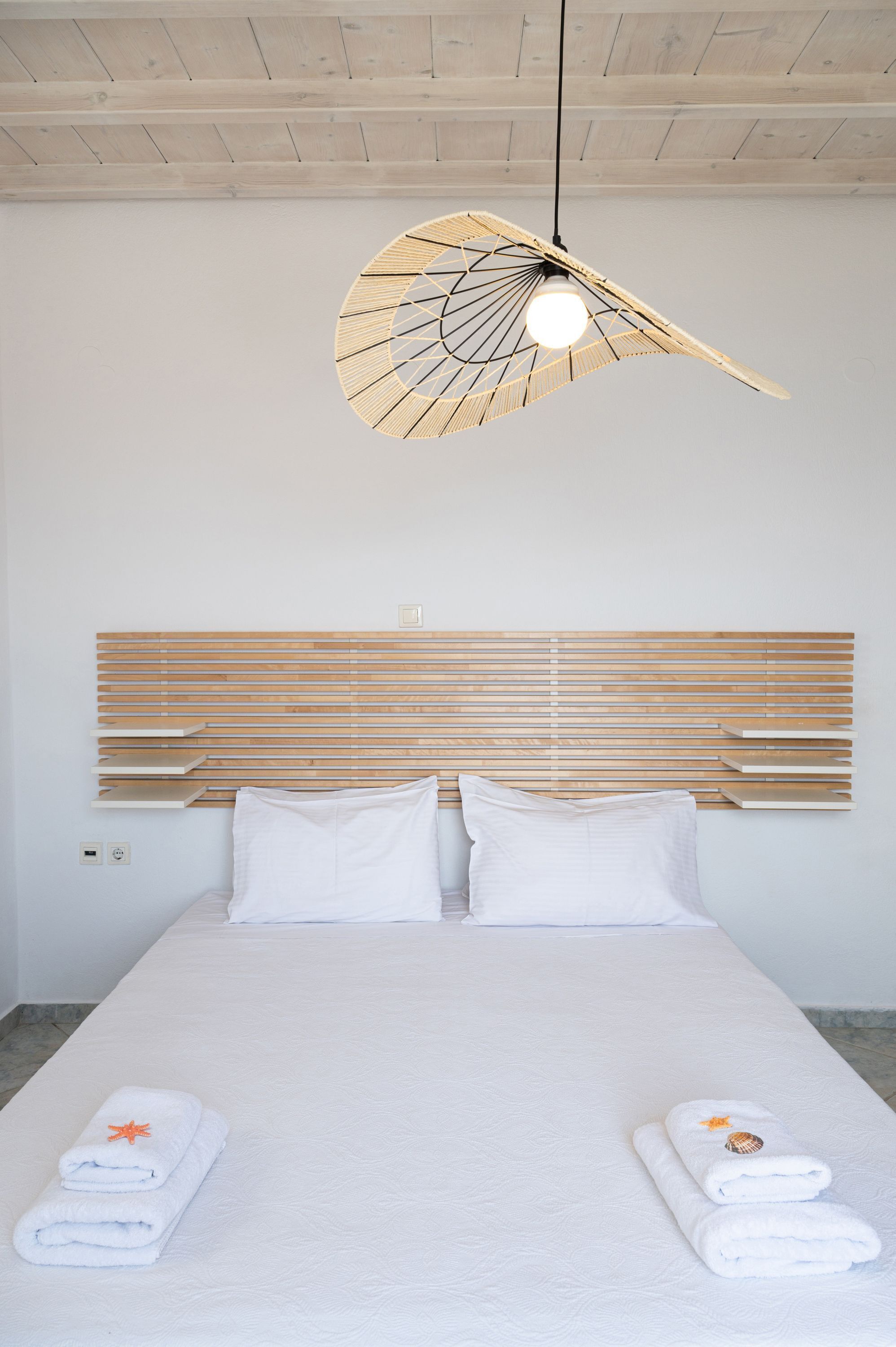 A hotel room with a bed, white linens, a wooden headboard, and a unique hanging light fixture.