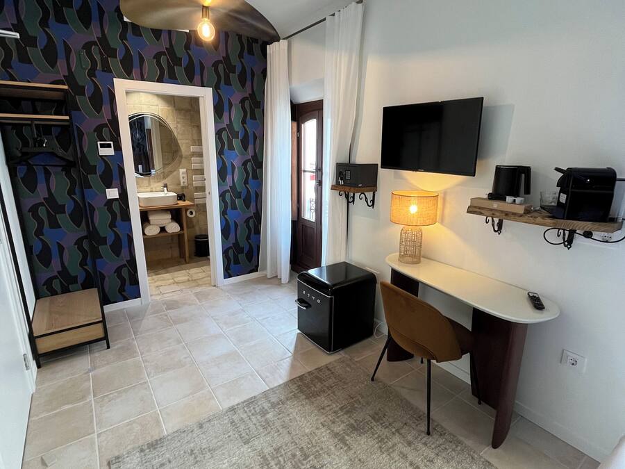 Una habitación de hotel moderna con baño, un escritorio con silla, un televisor montado en la pared y un pequeño estante con cafetera.