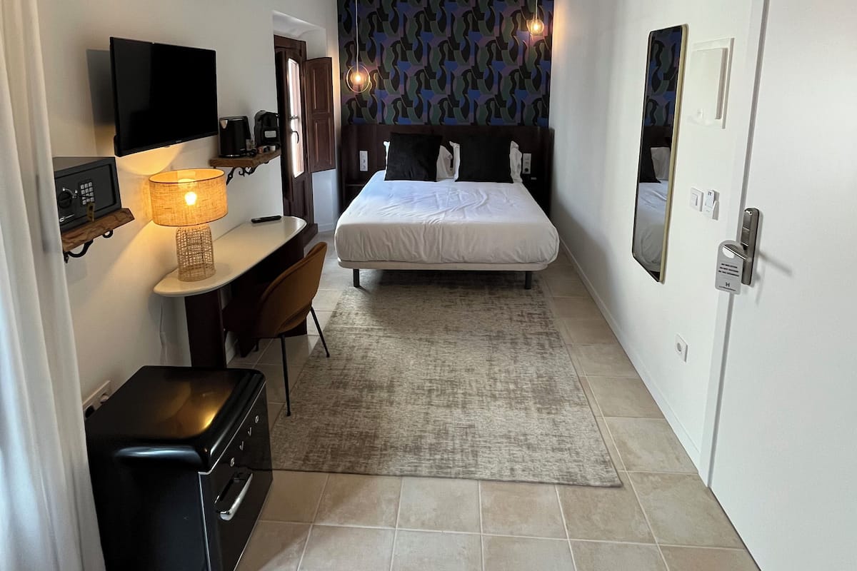 Een kleine hotelkamer met een bed, bureau, stoel en een televisie.