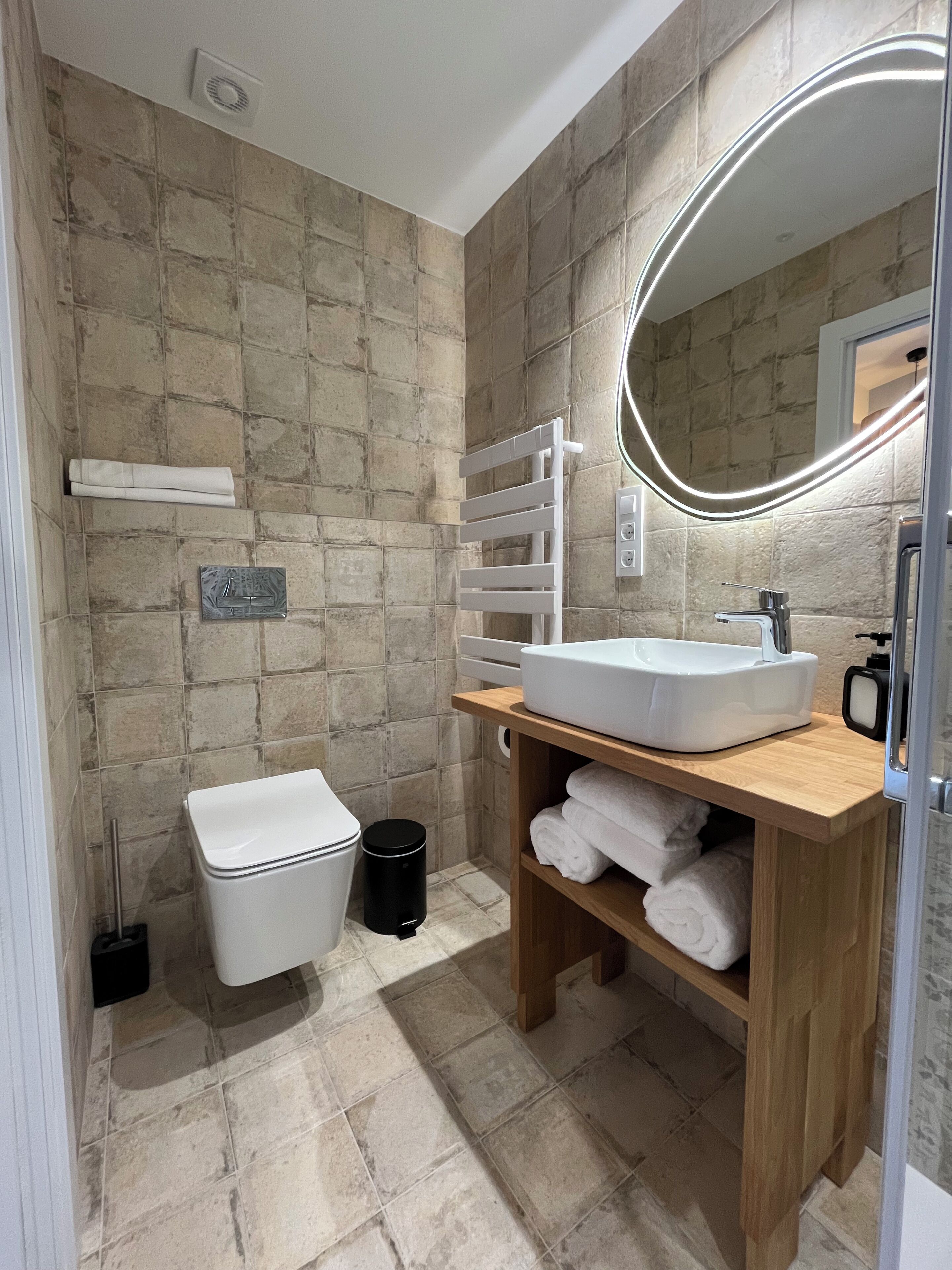 Un baño con inodoro blanco, tocador de madera con lavamanos blanco y espejo con luz.