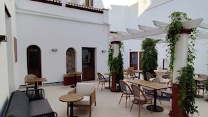 Une vaste terrasse extérieure dotée de plusieurs coins salon, dont un canapé et des tables, le tout entouré de murs blancs et agrémenté d’une pergola couverte de verdure.