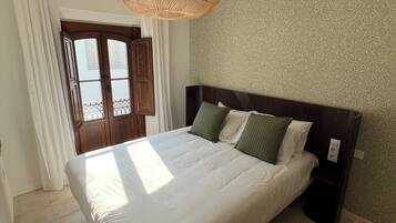 Een slaapkamer met een groot bed, een houten hoofdbord, een geweven lamp en een raam met gordijnen.