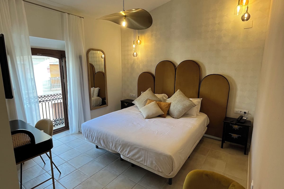 Een slaapkamer met een bed, nachtkastjes, een stoel, een bureau en een balkon met een hekwerk.