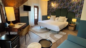 Une chambre d’hôtel moderne avec un escalier en colimaçon, un lit avec de nombreux oreillers, un canapé bleu, un bureau avec une lampe et un mur à motifs.