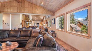 A spacious living area with a large leather sofa, a dining table, and a kitchen in the background.