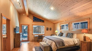 A bedroom with a wooden ceiling, a bed, a desk, and a window.