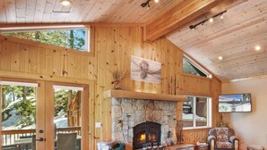 A cozy cabin interior with a stone fireplace, wooden walls, and a large window overlooking a snowy landscape.