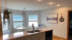 A kitchen with a central island, a dining area with a table and chairs, and a view of the outdoors through large windows. - Sunshine Escape: Spacious 6BR Home w/ Outdoor Oasis & Fire Pit, Near Marina (Monticello)