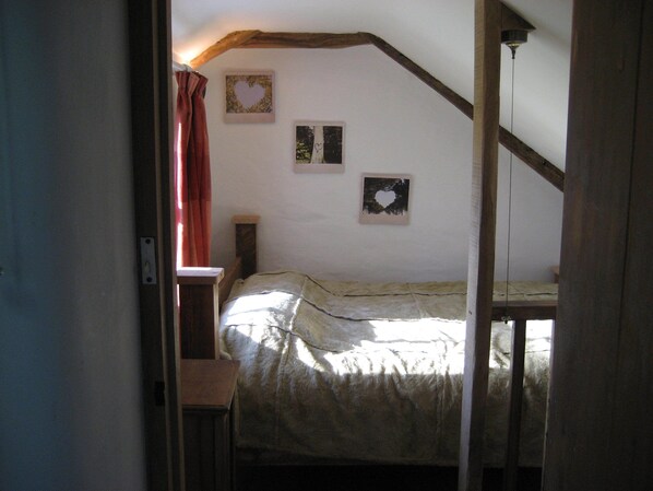 A narrow room with a bed, a window with red curtains, and three framed pictures on the wall.