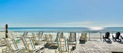 Un salon de plage doté de rangées de chaises longues rayées, toutes orientées vers l’océan, une piscine et une vue dégagée sur la plage.