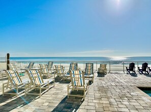 A beachside lounge with rows of striped lounge chairs facing the ocean, a pool, and a clear view of the beach.