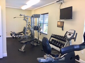 A gym with various exercise equipment including a bench press, dumbbells, and a weight machine.